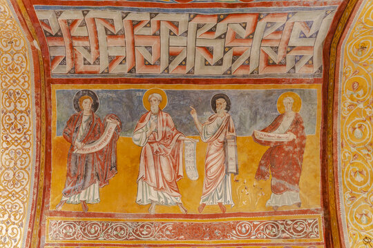 View of vibrant frescoes depicting figures with scrolls, adorned with golden halos and geometric patterns, paint a vivid historical narrative, Bominaco, Abruzzo, Italy.