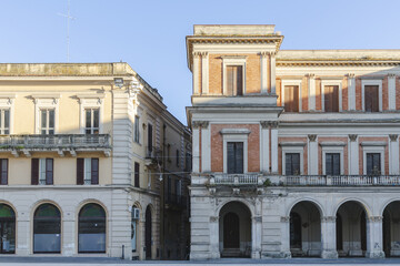 View of buildings standing tall with a blend of cream and brick hues under the tranquil sky, where arched entryways invite exploration, Chieti, Abruzzo, Italy.