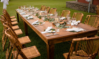 Mesa larga de madera con decoración natural y copas elegantes para evento al aire libre
