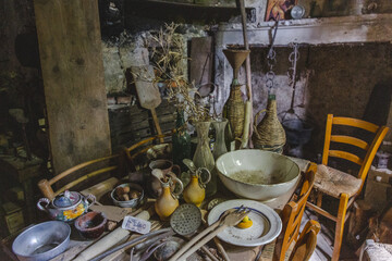 View of a rustic, cluttered wooden table laden with pottery, glassware, and cooking utensils in warm, earthy tones, Frattura Vecchia, Abruzzo, Italy.