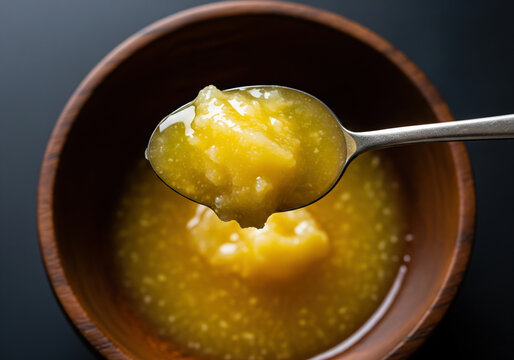 Golden liquid A2 cow ghee dripping from a spoon over a wooden bowl.
