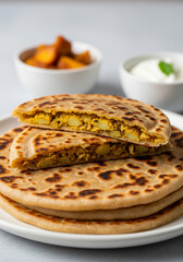 A stack of delicious aloo paratha with a perfectly cut top piece revealing the spicy potato filling. Served with yogurt and pickle