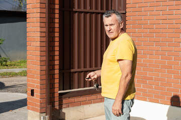 Senior man in yellow t-shirt holding keys and remote control fob to open automatic gate