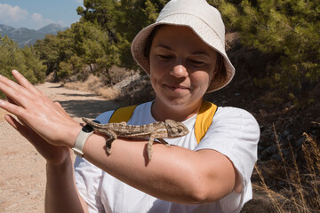 woman holds on hand wild chameleon lizard. tourist hiking Lycian Way in Turkey