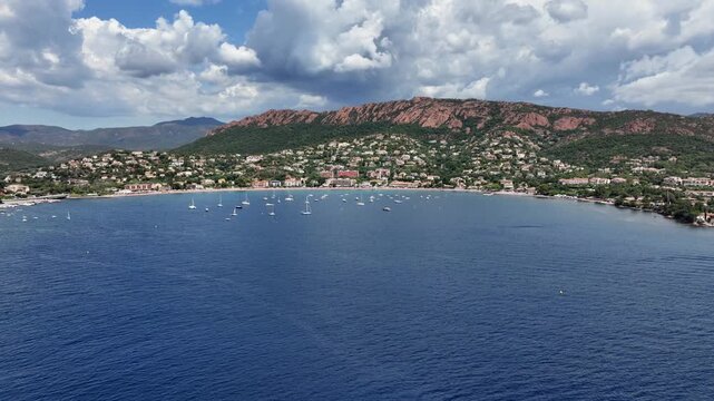 flying across Agay Bay, French Riviera (C&ocirc;te d'Azur) with Beach  "Agay Plage" cityscape of Saint-Rapha&euml;l and bright red mountains from "Massif de l'Esterel" in background - 4k aerial video footage