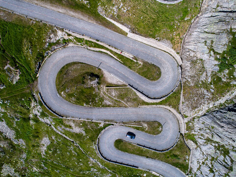 Aerial view of a snaking road cutting through the rugged, rocky landscape, with vibrant green patches contrasting against the grey stone, Gotthard Pass, Ticino, Switzerland.