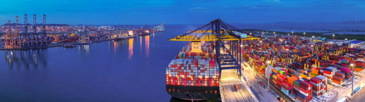 Aerial view of international cargo containers ship at industrial import-export port prepare to load containers with big container loader ship vessel at night. global transportation, logistic business.