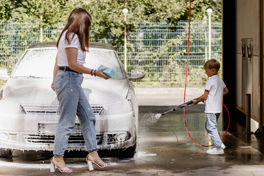 Happy mother and son washing a white car together with sponges and foam at self-service car wash, bonding activity on a summer day - Powered by Adobe