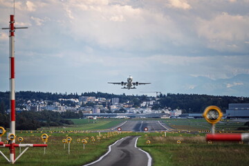 Commercial passenger plane taking off from a long runway, front view. Overcast summer day, runway edge lights, super telephoto close up view, no people