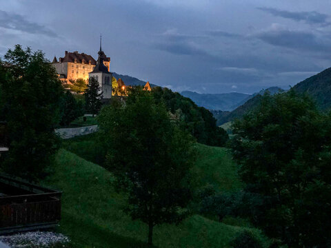 View of the illuminated Gruy&Atilde;&uml;res Castle perched atop a lush green hill under a twilight sky, a beacon of history and beauty, Gruy&Atilde;&uml;res, Fribourg, Switzerland.