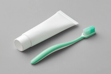 A tube of toothpaste paired with a mint-green toothbrush, both arranged on a smooth, gray surface. Cleanliness and oral health essentials.