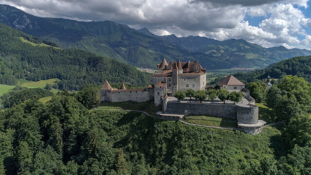 Aerial view of the medieval Gruy&Atilde;&uml;res Castle perched atop a verdant hill, its stone walls and red-tiled roofs contrasting against the backdrop of the majestic Alps, Gruy&Atilde;&uml;res, Fribourg, Switzerland.