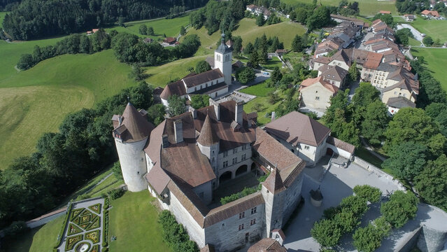 Aerial view of the Gruy&Atilde;&uml;res Castle with its imposing towers and red roofs next to a church, standing proudly amidst green hills, Gruy&Atilde;&uml;res, Fribourg, Switzerland.