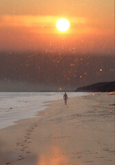 Sunrise or sunset over the sea. Footprints in the sand, a man walking on the beach.