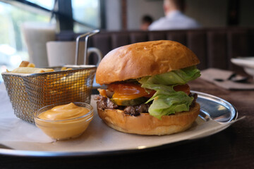 A delicious juicy burger and fries on a table in a cafe. NOT healthy food.
