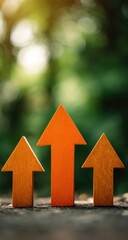 Three orange wooden arrows pointing upward against a blurred natural background