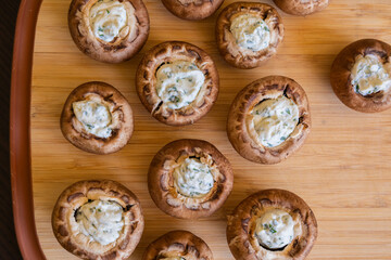 raw champignon mushrooms stuffed with herb cream cheese, arranged on a tray and ready to bake