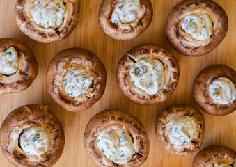 raw champignon mushrooms stuffed with herb cream cheese, arranged on a tray and ready to bake