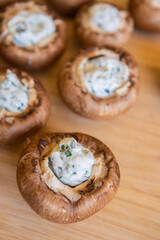 raw champignon mushrooms stuffed with herb cream cheese, arranged on a tray and ready to bake