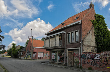 Deserted street in Doel, Belgium showing abandoned residential buildings with boarded windows and graffiti under cloudy sky.