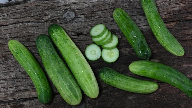 cucumber (Cucumis sativus) and slices on wood background. Freshly sliced mini cucumbers with knife on wooden cutting board.