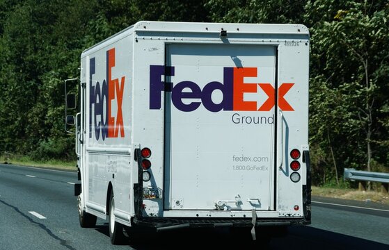 Virginia, U.S.A - Sep 2, 2025 - A FedEx Ground truck travels down a highway, its distinctive logo clearly visible against the green foliage.