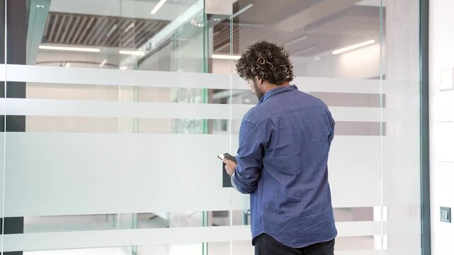 Young businessman unlocking glass door using mobile phone application, opens and enters modern office. Scanning open smartphone with mock up screen app. Smart electronic locks with keyless access