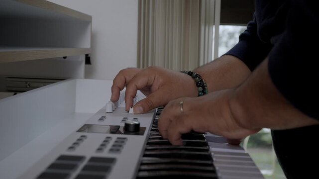 Close-up of a producer's hands playing a white midi keyboard and adjusting knobs. Creative process of composing music in a home studio