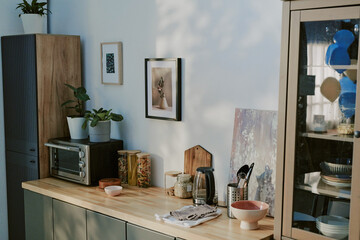 Modern kitchen countertop displaying electric toaster oven, electric kettle, glass jars with pasta, potted plants, bowls, utensils, framed wall art, wooden cutting board