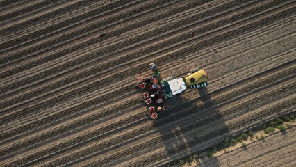 Aerial view of modern tractor with planter and seed applicator working in a freshly plowed field during daytime symbolizing agricultural technology and crop cultivation