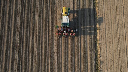 Aerial View of a Tractor Planting Seeds in Rows on a Cultivated Agricultural Field Under the Warm Golden Light of Sunset