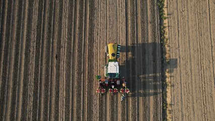 Aerial view of agricultural machinery planting crops in a vast cultivated field under the bright sun casting long shadows across the land showcasing modern farming techniques and rural landscape