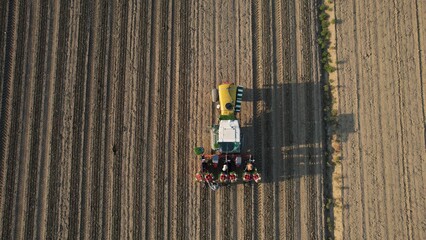 Agricultural tractor planting seeds in a vast field from an aerial perspective showcasing modern farming technology and the vastness of cultivated land at sunrise casting long shadows