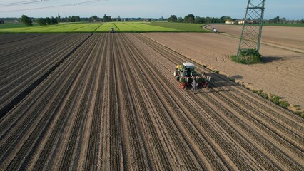 Agricultural tractor planting seeds in a vast plowed field with rows of soil ready for cultivation under a clear blue sky on a sunny day
