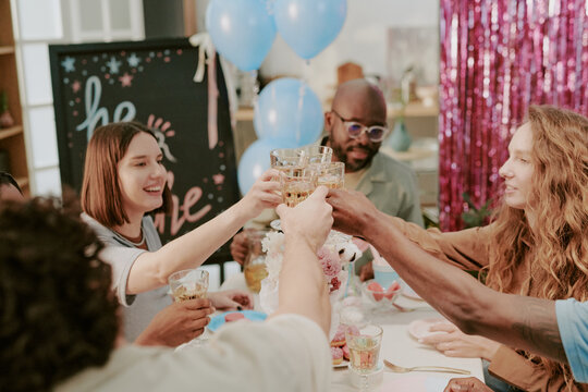 Diverse group of young adults and middle aged people raising glasses in celebratory toast at decorated table, smiling and interacting together during festive gathering indoors