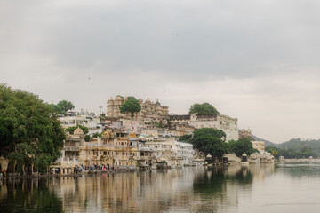 Fototapeta premium Cityscape Reflecting on Water: A scenic view of an urban area with historic architecture, gracefully reflected in the calm waters under a cloudy sky.
