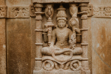 Ancient sandstone carving of a seated deity, intricate stonework details, part of a temple wall, cultural heritage, spiritual art.