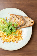 Scrambled eggs, sliced avocado, arugula, and sourdough toast on a plate