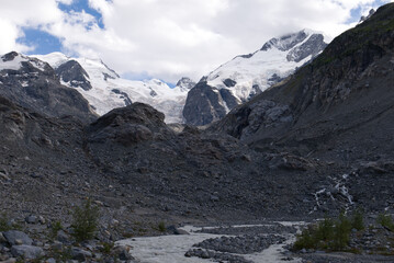 Morteratsch Glacier, Switzerland. Alpine panorama of a glacial valley with a rocky riverbed and snow-capped peaks in the Swiss Alps. Mountain landscape, river, and cloudy sky. Glacial terrain.