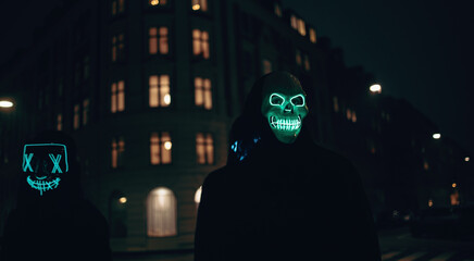 Fototapeta premium Two individuals wearing glowing masks on an urban street at night