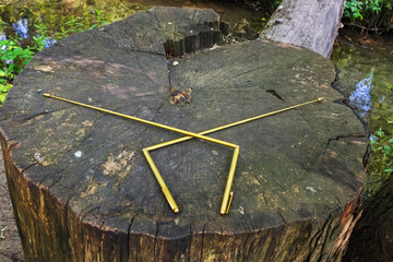 Two dowsing rods for the radiesthesia technique, lie on the stump of an old tree. Dowsing with metal indicator L rods is a modern tool of a dowser. An ancient method, not scientifically proven