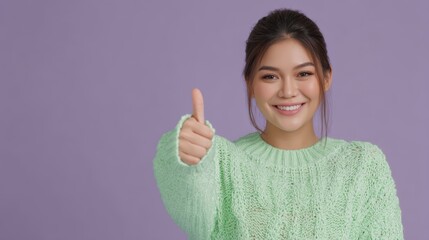 A smiling woman in a mint green sweater gives a thumbs-up against a purple background, conveying positivity and confidence, asian office girl with good job expression