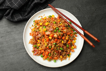 Delicious fried rice with vegetables and chopsticks on grey textured table, top view