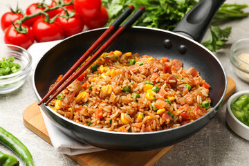 Delicious fried rice in frying pan and chopsticks on grey table, closeup