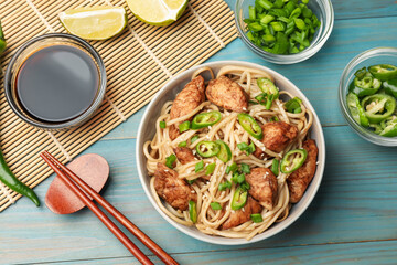 Tasty noodles with chicken, green peppers and sesame seeds served on blue wooden table, flat lay