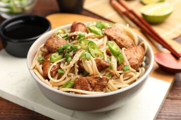 Tasty noodles with chicken, green peppers and sesame seeds served on wooden table, closeup