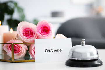 Card with word Welcome, desk bell and roses on white table, closeup