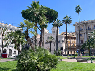 Palmen und historische Architektur in Rom an einem sonnigen Tag. Stadtpark mit gr&uuml;ner Wiese, B&auml;nken und mediterraner Atmosph&auml;re, ideal f&uuml;r Reise, Italien und Architekturthemen.