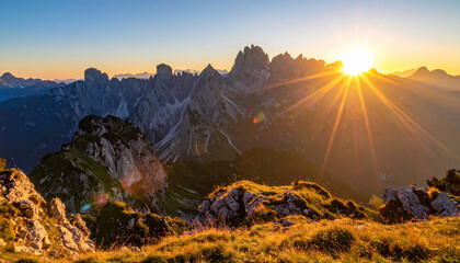 Sunset over rocky mountain range with golden light illuminating grassy foreground and rugged peaks in distance, creating warm and peaceful natural landscape