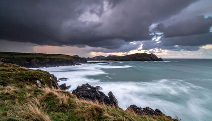 Stormy coastal landscape with dark clouds over rocky cliffs and turbulent sea, creating dramatic and moody atmosphere with soft waves and grassy foreground